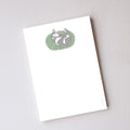 A Cozy Kitty Notepad featuring an illustrated grey and white cat curled up on a patterned rug, containing unlined pages.