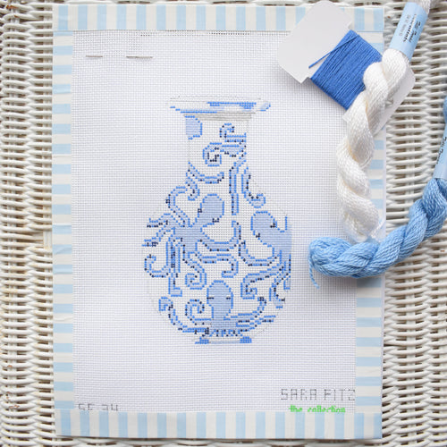 A partially completed Octopus Ginger Jar Needlepoint by Sara Fitz is shown on white 18 mesh canvas, with blue and white threads in the corner, all resting on a striped woven background.