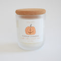 The Sara Fitz Pumpkin Cashmere Candle comes in a frosted glass jar with a cork lid and features a label decorated with a pumpkin and anchor illustration. Hand-poured in Maine, this candle is made from premium coconut soy wax for a clean, cozy burn and showcases the inviting scents of pumpkin, clove, caramel, and cashmere.