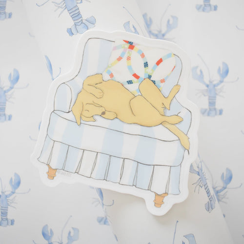 The "Pup in a Chair Sticker" by Sara Fitz features a yellow dog lying upside down on a light blue and white striped armchair with colorful pillows, set against a white background with blue lobster illustrations. Weatherproof vinyl.