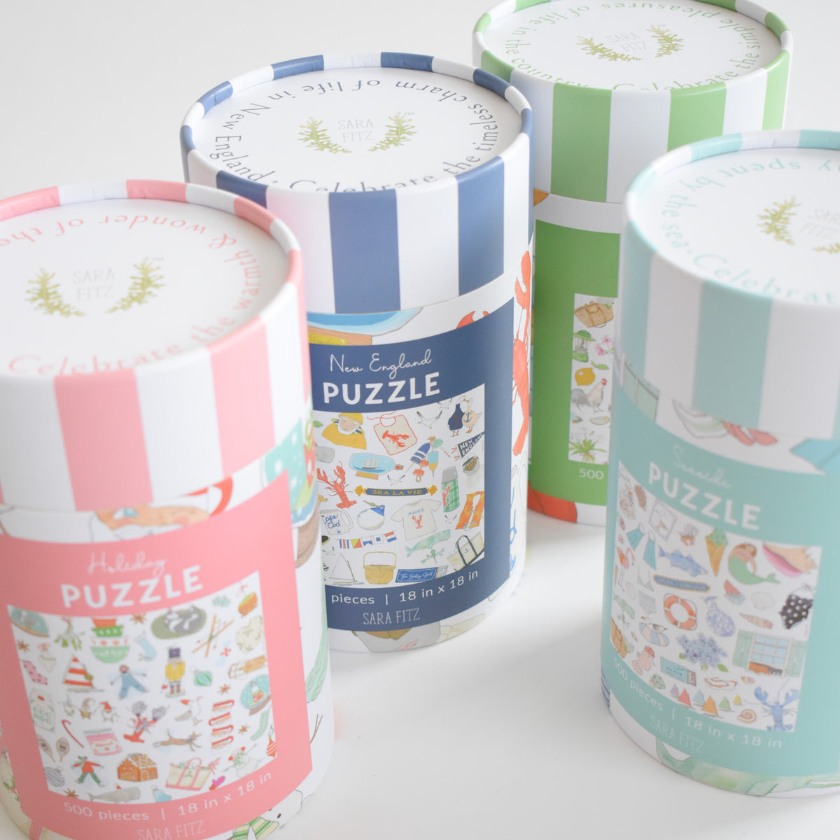 Four cylindrical New England Puzzle boxes with patterned lids and illustrated labels featuring themed icons for a 500-piece puzzle.