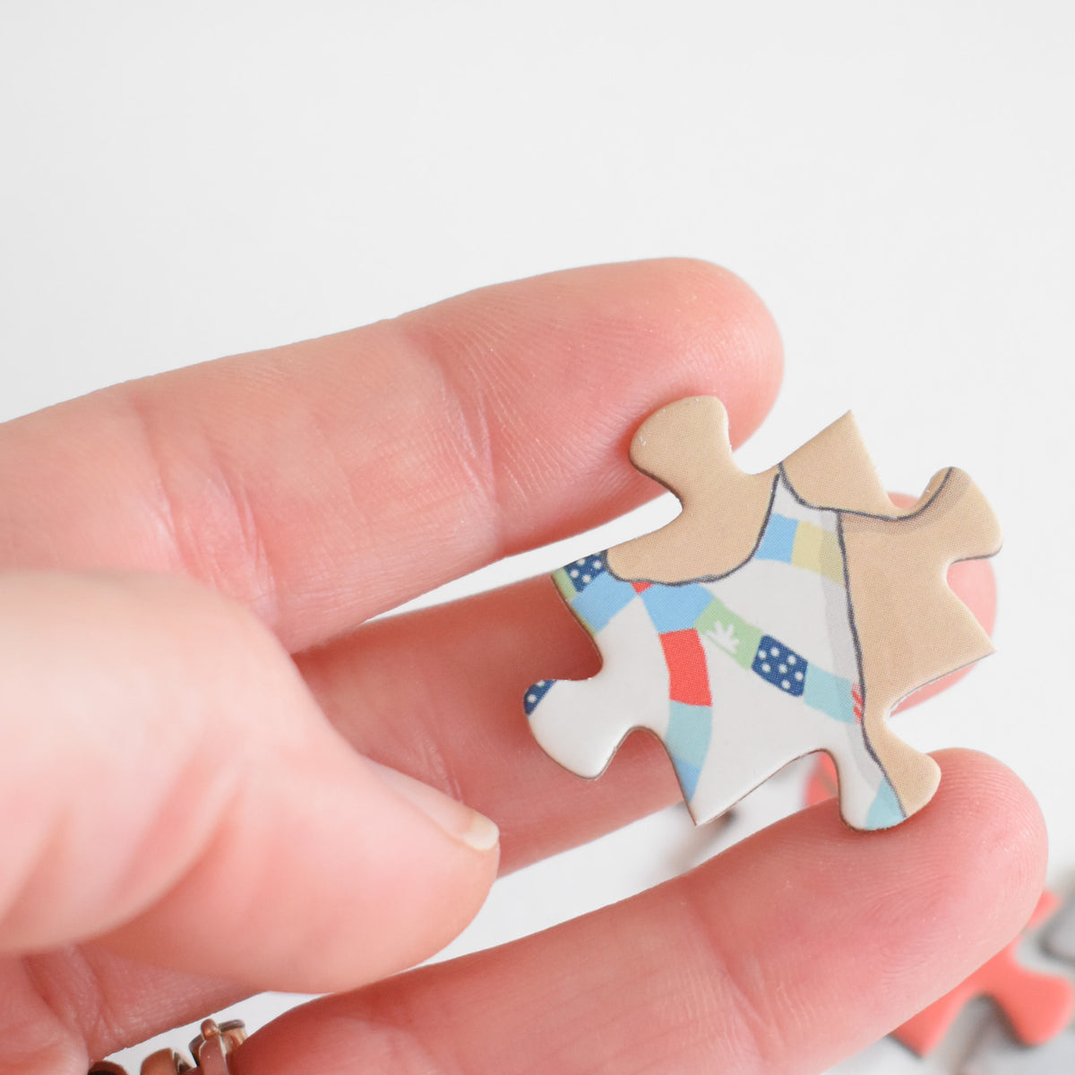 A hand holds a piece of a Countryside Puzzle, a vintage collage jigsaw featuring a pattern of colorful, patterned fabric squares.