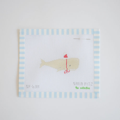 The MINI Santa Whale Needlepoint by Sara Fitz features a light-colored whale in a red hat and scarf on white canvas with blue stripes. "Sara Fitz" branding appears on the design, and a needle is placed at the top right.