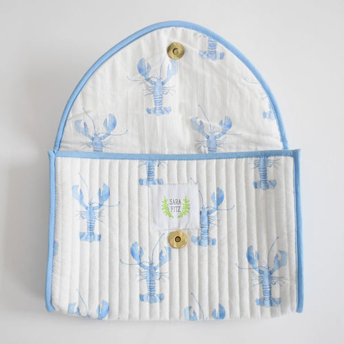 The Clutch, Blue Lobster by Sara Fitz is a quilted, handmade pouch from India with white fabric, blue trim, and light blue lobster patterns. It has a brass snap button and features the Sara Fitz label with a green leaf logo inside.