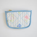 The Sara Fitz Coin Pouch, Cross Stitch Floral, is a quilted cotton card holder with a light blue border and zip closure, featuring pastel cross-stitched florals on white.