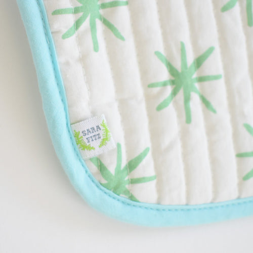 A close-up of the Sara Fitz Coin Pouch, Green Star shows a white cotton quilted bag with light green starburst patterns, a blue border, and a small fabric tag labeled Sara Fitz in green and blue.
