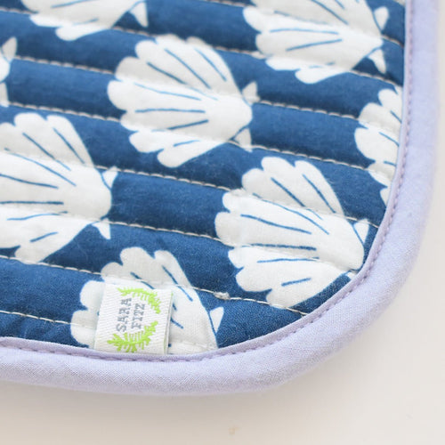 A close-up of the Sara Fitz Coin Pouch, Shells: a cotton quilted bag with white petal-like patterns on blue, light purple border, and small white tag with green text, handmade in India.
