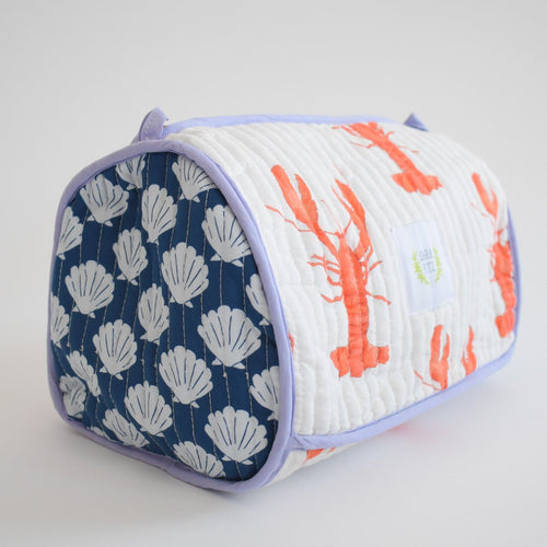 The Sara Fitz Cosmetic Pouch, Lobster, is a quilted cotton toiletry bag with purple trim, orange lobsters on white, and white shells on navy blue. This rectangular travel organizer includes a small side handle.