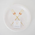 The Sara Fitz Oar Paper Dessert Plates set includes 24 white 7-inch plates with two crossed paddles in red and yellow accents, packaged in clear plastic.