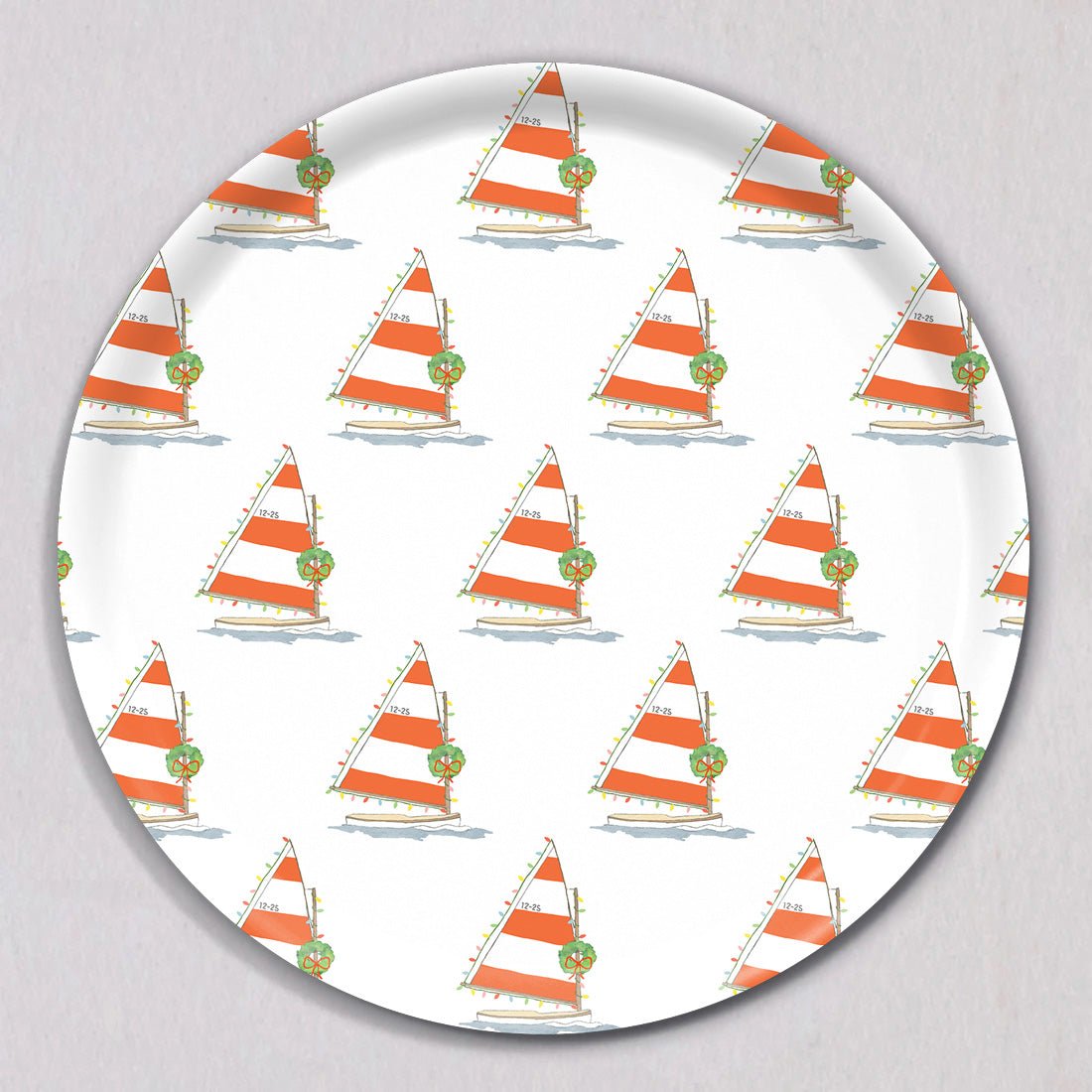 Large Holiday Sailboat Tray, Round, featuring a repeating pattern of sailboats with orange and white striped sails, decorated with Christmas wreaths and string lights on a melamine coated birch wood surface.