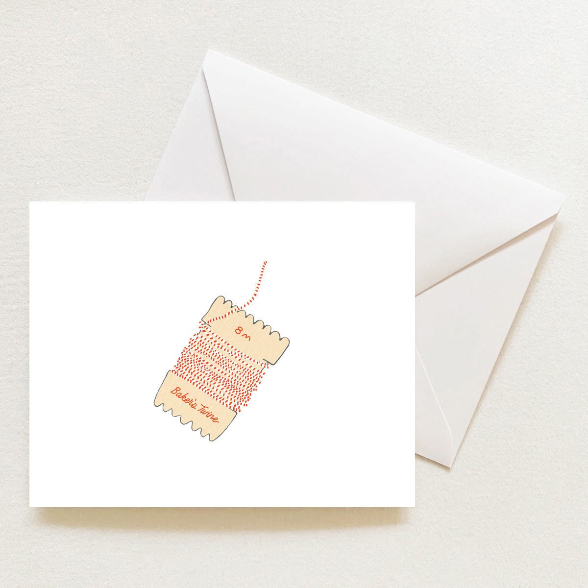 A Holiday Trimmings Note Card from this boxed set features an illustration of red and white bakers twine on a cardboard spool, with a white envelope tucked behind it.