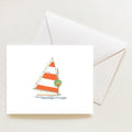A Sara Fitz Holiday Sailboat Note Card boxed set featuring an illustration of a sailboat with orange and white striped sails decorated with Christmas lights and a wreath, resting above an envelope.