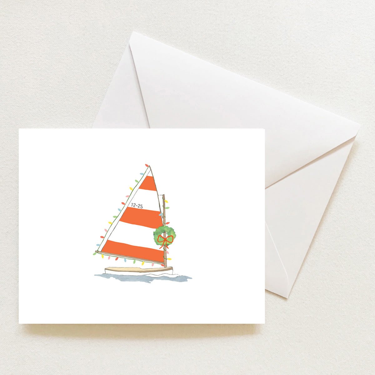 A Sara Fitz Holiday Sailboat Note Card boxed set featuring an illustration of a sailboat with orange and white striped sails decorated with Christmas lights and a wreath, resting above an envelope.