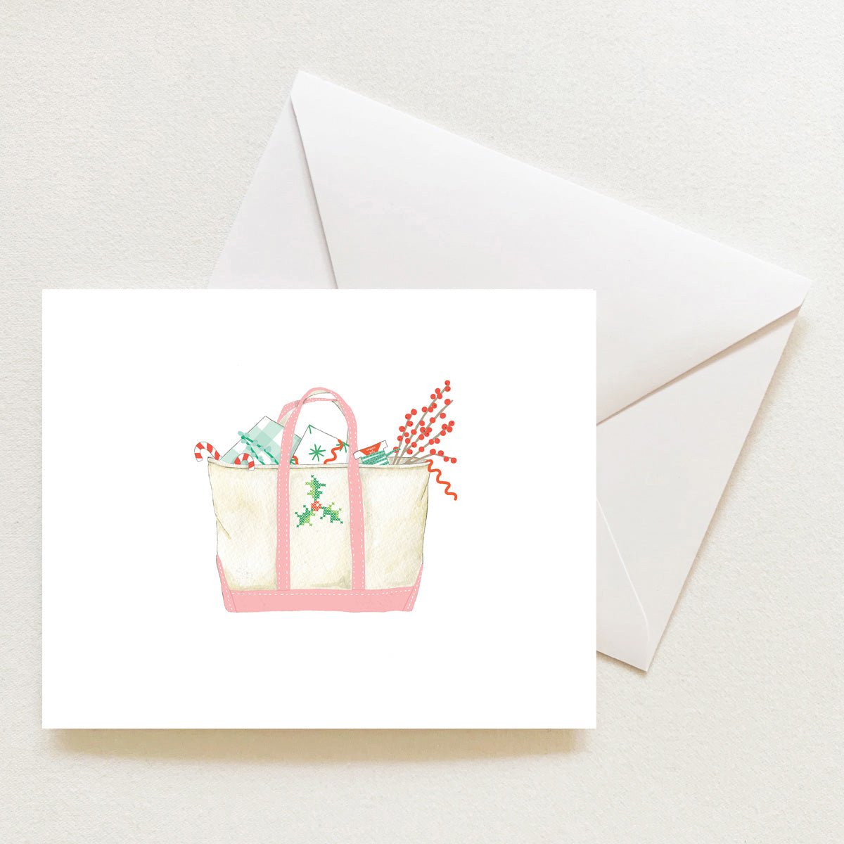 A Holiday Tote Note Card from Sara Fitz featuring a watercolor illustration of a canvas tote bag filled with holiday items, including candy canes and berries, shown with a matching envelope.