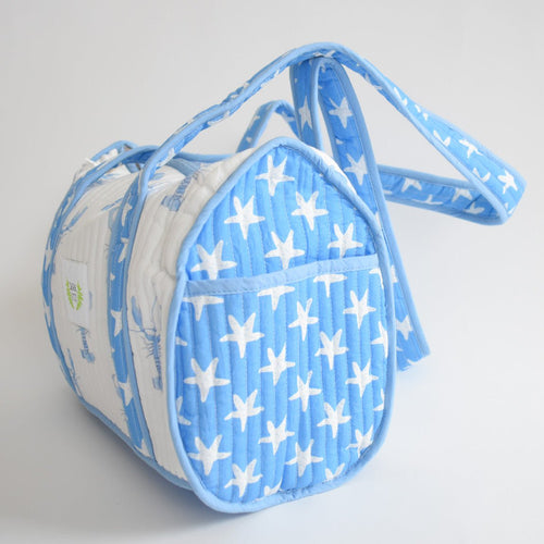 The Purse, Blue Lobster by Sara Fitz is a small, cylindrical cotton shoulder bag with a blue and white star pattern, quilted texture, long strap, and rounded ends, handmade in India and shown on a white background.