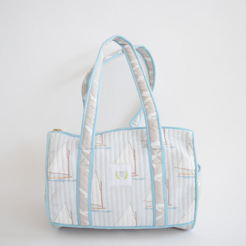 The Sara Fitz Purse, Sailboat is a handmade quilted shoulder bag from India with light blue trim and handles, featuring a sailboat pattern on white, shown against a plain white background.