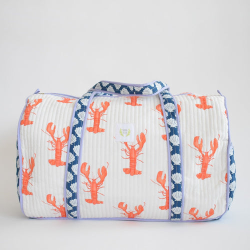 The Sara Fitz Weekender Tote, Lobster, is a spacious cotton travel bag with a white background, orange lobster print, and blue-and-white shell-patterned handles—perfect for your next stylish getaway.