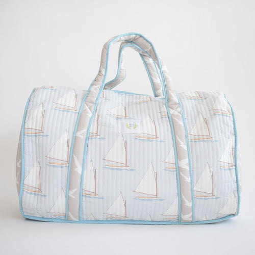 The Sara Fitz Weekender Tote, Sailboat, is a quilted cotton travel bag with light blue piping, sailboat and seagull prints on white, two handles, and a small white front label.