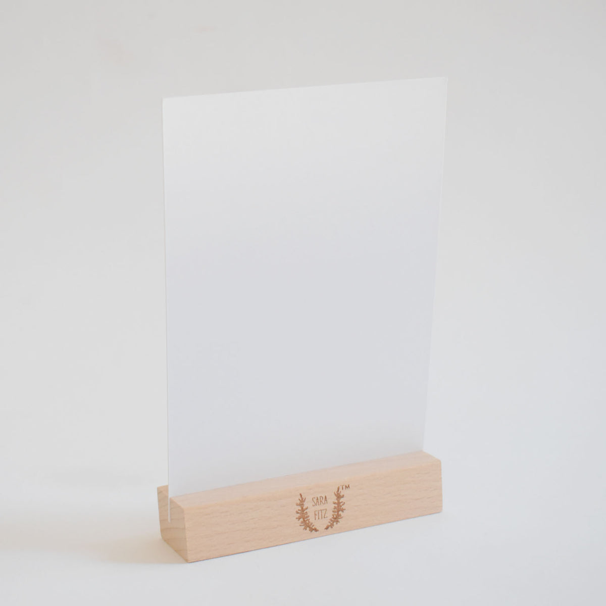 A blank white Sara Fitz 2027 Desk Calendar card held upright in a small wooden stand.