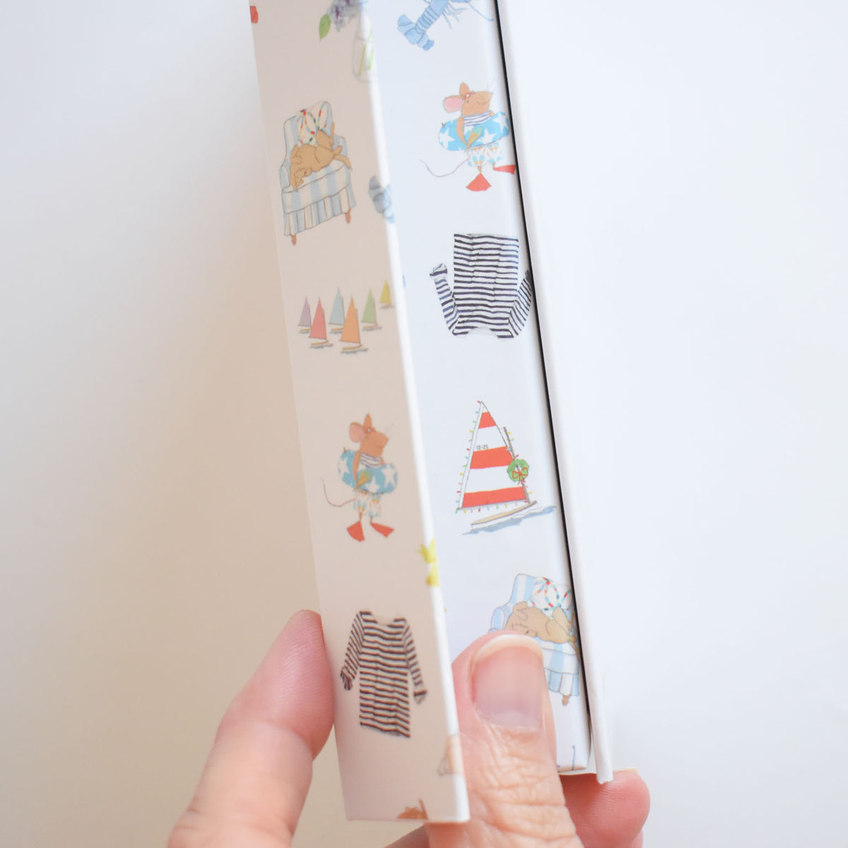 A hand holds a 2027 Desk Calendar featuring a white cover with Sara Fitz illustrations of mice, sailboats, and striped shirts.