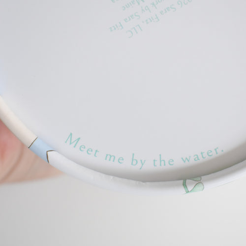 The interior rim of the Seaside Puzzle container features the text Meet me by the water printed in light blue.