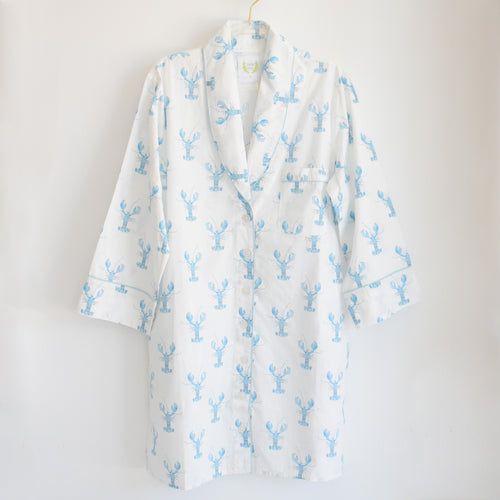 The Blue Lobster Sleep Shirt by Sara Fitz, featuring long white cotton sleeves and a playful blue lobster print, hangs on a gold hanger against a plain white background—bringing the perfect touch of whimsy to women’s sleepwear.