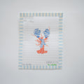 The Small Cozy Lobster Needlepoint by Sara Fitz features an orange and blue striped lobster on white canvas with light blue and white borders. “SARAH FITZ the collection” is stitched at the bottom. 18 mesh canvas only.