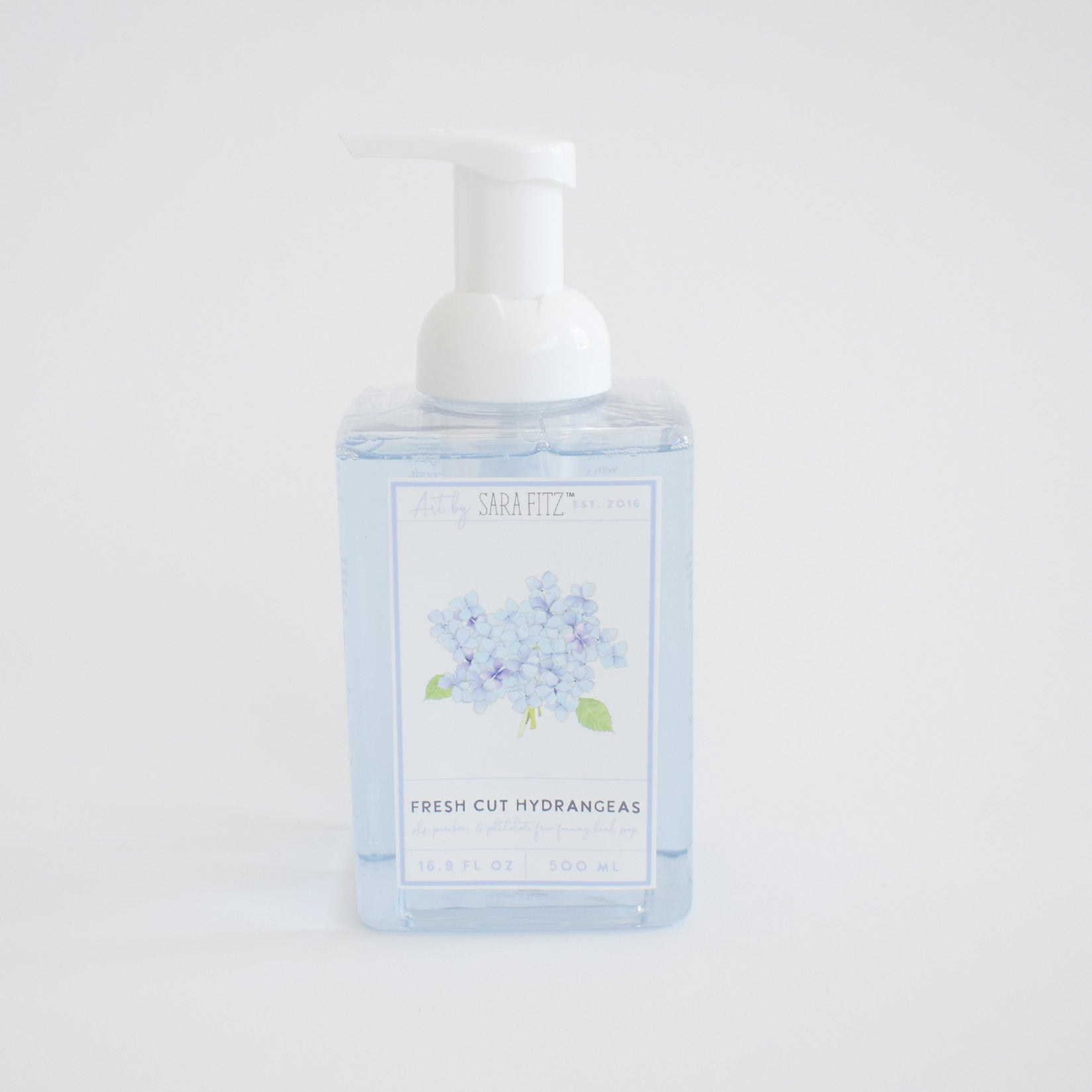 A clear pump bottle labeled Sara Fitz Foaming Soap Hydrangea, filled with light blue foam soap and decorated with blue hydrangea artwork. Non-toxic and inspired by fresh cut hydrangeas.