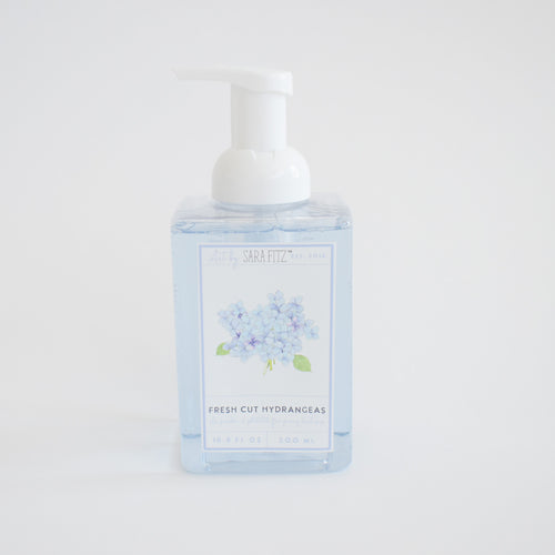 A clear pump bottle labeled Sara Fitz Foaming Soap Hydrangea, filled with light blue foam soap and decorated with blue hydrangea artwork. Non-toxic and inspired by fresh cut hydrangeas.