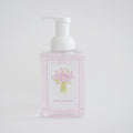 A clear pump bottle of Sara Fitz Foaming Soap Peony, filled with light pink, non-toxic liquid and adorned with a floral illustration, is displayed against a plain white background.