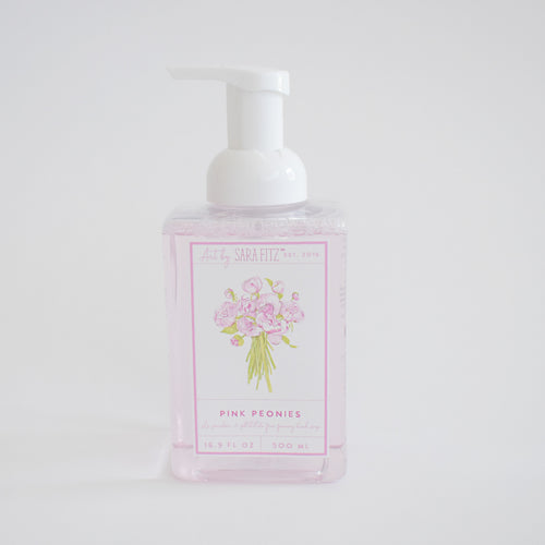 A clear pump bottle of Sara Fitz Foaming Soap Peony, filled with light pink, non-toxic liquid and adorned with a floral illustration, is displayed against a plain white background.