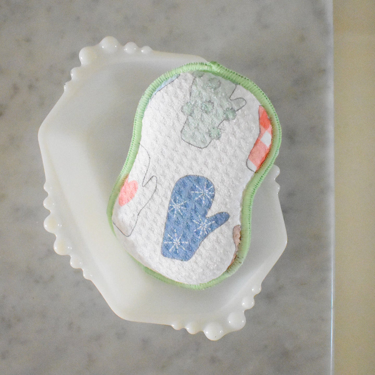 A textured, hourglass-shaped Re:usable Sponge, Mittens resting on a small white dish.
