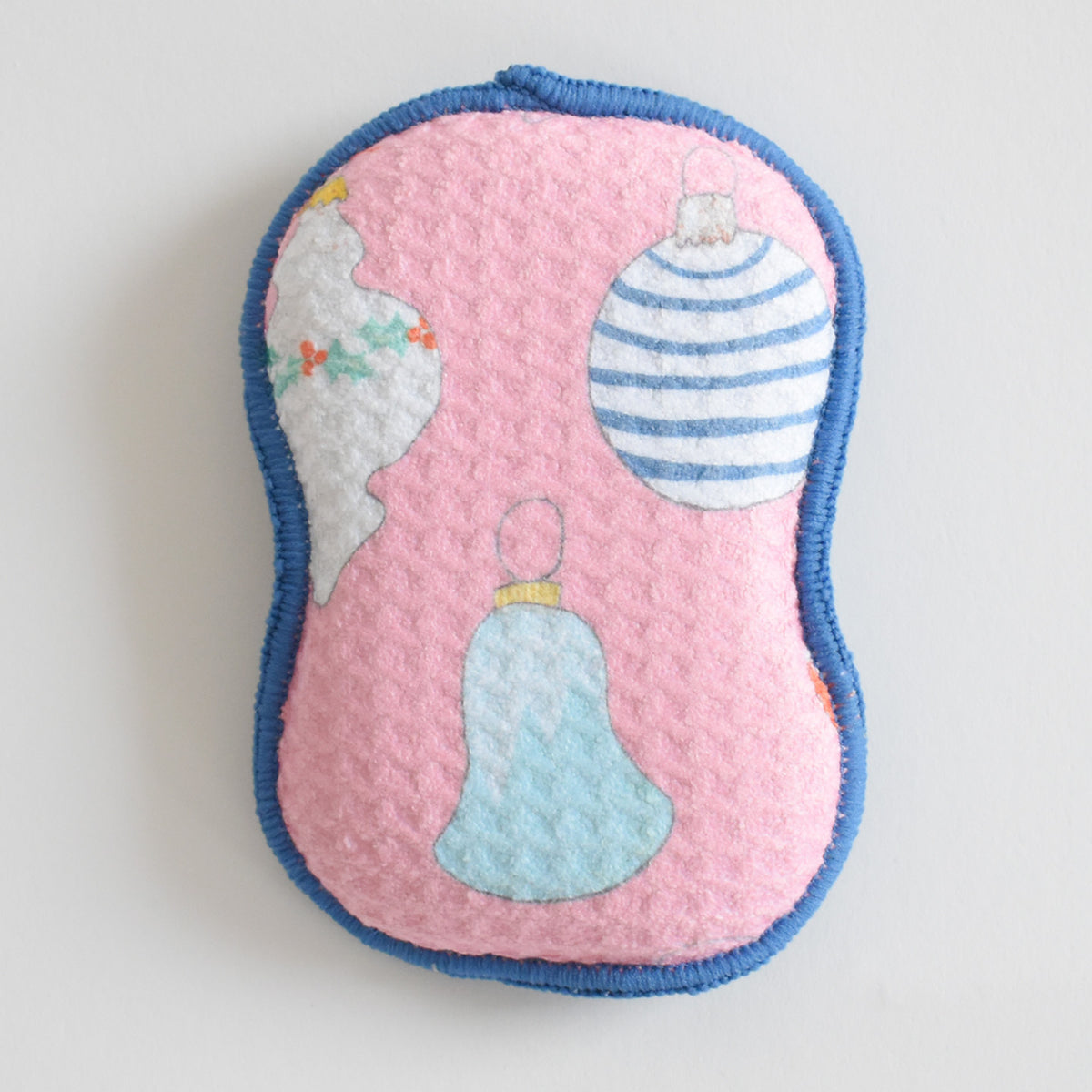 Sara Fitz Re:usable Sponge, Ornament, featuring a pink washable sponge with a blue trim decorated with illustrations of Christmas ornaments.