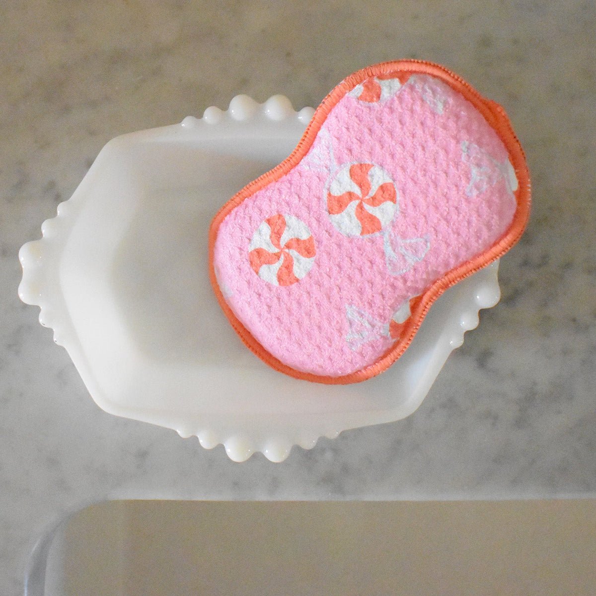 A pink, contoured Re:usable Sponge, Peppermint resting in a white scalloped soap dish.