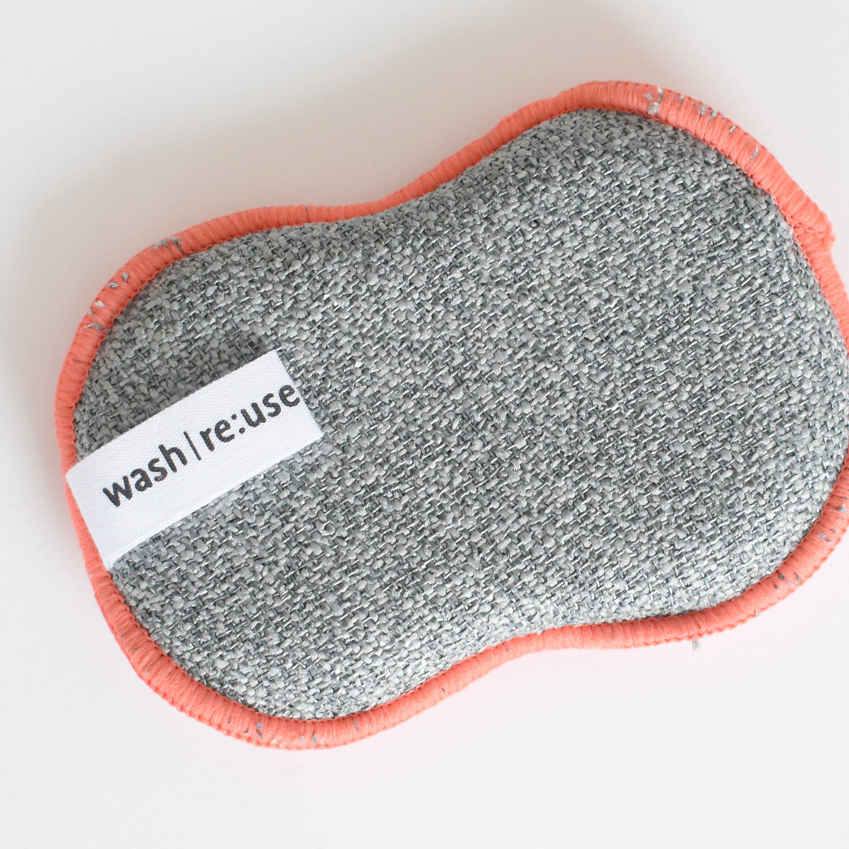 Gray oval Re:usable Sponge, Peppermint with an orange stitched edge and a white tag that reads wash | re:use.