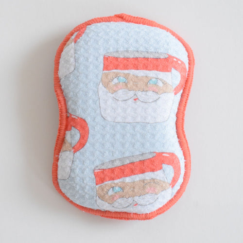 Hourglass-shaped Re:usable Sponge, Santa Mug, with a repeating light blue pattern of Santa Claus mugs and a coral-colored fabric edge.