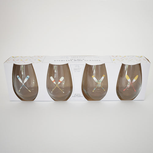 Set of four 20 oz clear stemless wine glasses, each with two crossed colorful oars. Packaged in a white box with a geometric pattern and the Sara Fitz brand name centered on top. Product: Stemless Wine Glasses, Oar by Sara Fitz.