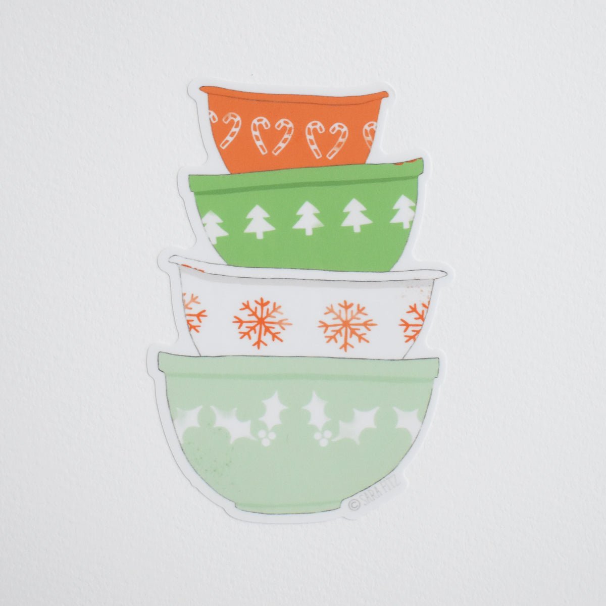 A Sara Fitz Mixing Bowls sticker featuring a stack of four colorful bowls decorated with Christmas patterns including candy canes, pine trees, and snowflakes.