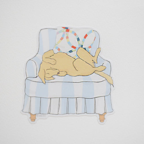 The Pup in a Chair Sticker by Sara Fitz features a yellow dog lounging upside down on a blue and white striped armchair with a colorful pillow—a playful, weatherproof vinyl sticker made in the USA.