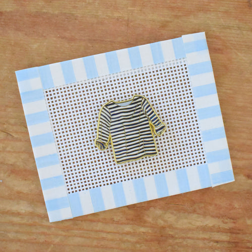 The Striped Shirt Needle Minder by Sara Fitz is shown on a needlepoint canvas with a blue gingham border and striped sweater design—an ideal match for your favorite stitching accessories.