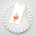 Santa Fitz Tags featuring an illustration of Santa Claus carrying a sack, attached to yellow and white baker’s twine and resting on a white scalloped dish.