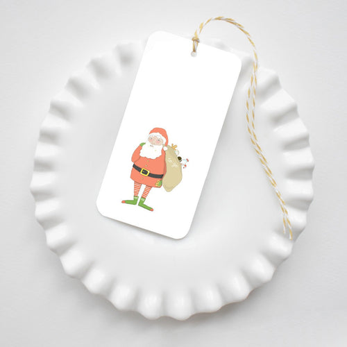 Santa Fitz Tags featuring an illustration of Santa Claus carrying a sack, attached to yellow and white baker’s twine and resting on a white scalloped dish.