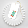 Holiday Trimmings Tags are rectangular gift tags tied with yellow and white baker’s twine, featuring an illustration of a green ribbon spool labeled jolly and 2yd cotton.