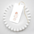 The Sara Fitz Seahorse Tags feature a pastel seahorse design on a white rectangular tag, tied with yellow and white baker's twine. Presented on a ruffled-edge plate, these tags add a charming touch to any size gift.