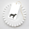 The Sara Fitz Black Pup Tags feature a black dog with a green collar on a white tag, attached with gold and white baker’s twine and shown resting on a white scalloped-edge plate.