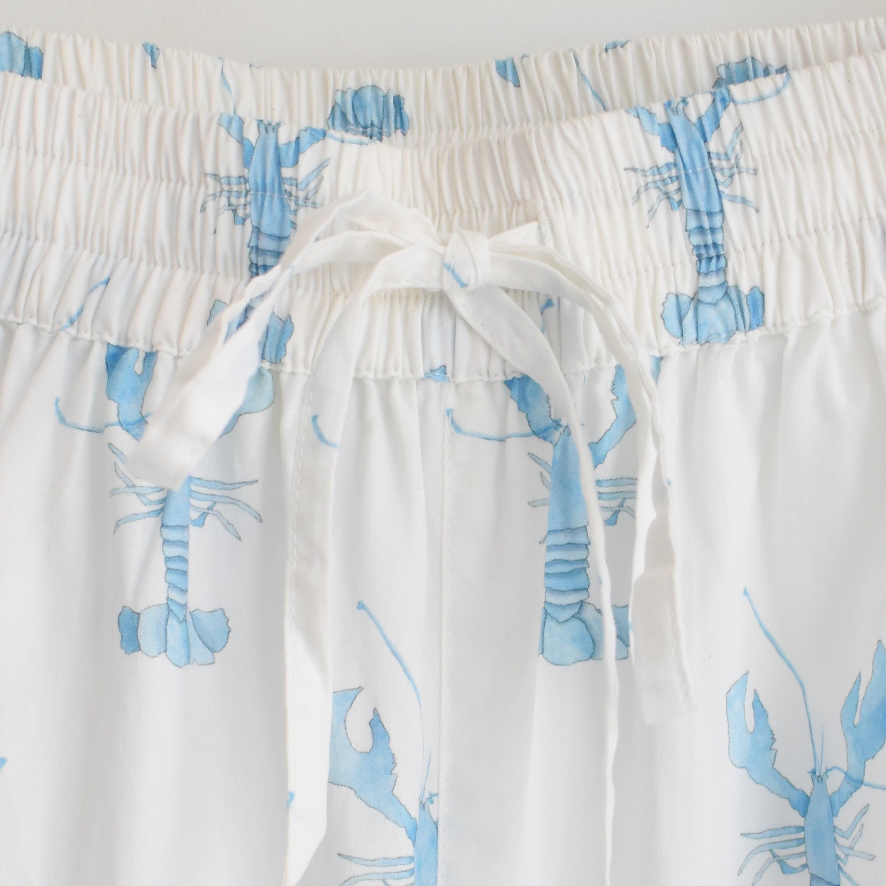 Close-up of white shorts from the Sara Fitz Blue Lobster Short Pajama Set, designed with a drawstring waistband and decorated with a light blue lobster pattern. These coastal pajamas are perfect for relaxing in style.