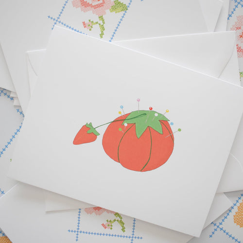 The Sara Fitz Tomato Pincushion Note Card is a unique, eco-friendly boxed stationery set featuring an illustrated red tomato pincushion with colorful pins—perfect for any occasion.