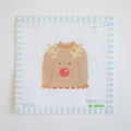 The Sara Fitz Ugly Sweater Needlepoint is a stitch-painted 18 mesh canvas featuring a brown reindeer sweater with a red nose and yellow antlers on a blue and white striped border.