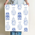 A person holds a square sheet of Sara Fitz Nautical Ginger Jar Wallpaper, which features rows of blue and white decorative vases and jars with unique designs on a white background.