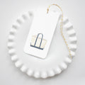 The Sara Fitz Canvas Tote Tags feature a tote bag illustration and come with gold and white baker's twine, creating a charming accent for your gift wrapping. Shown here on a white, wavy-edged plate.